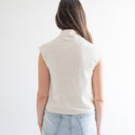 back view of woman wearing cream sleeveless mockneck sweater