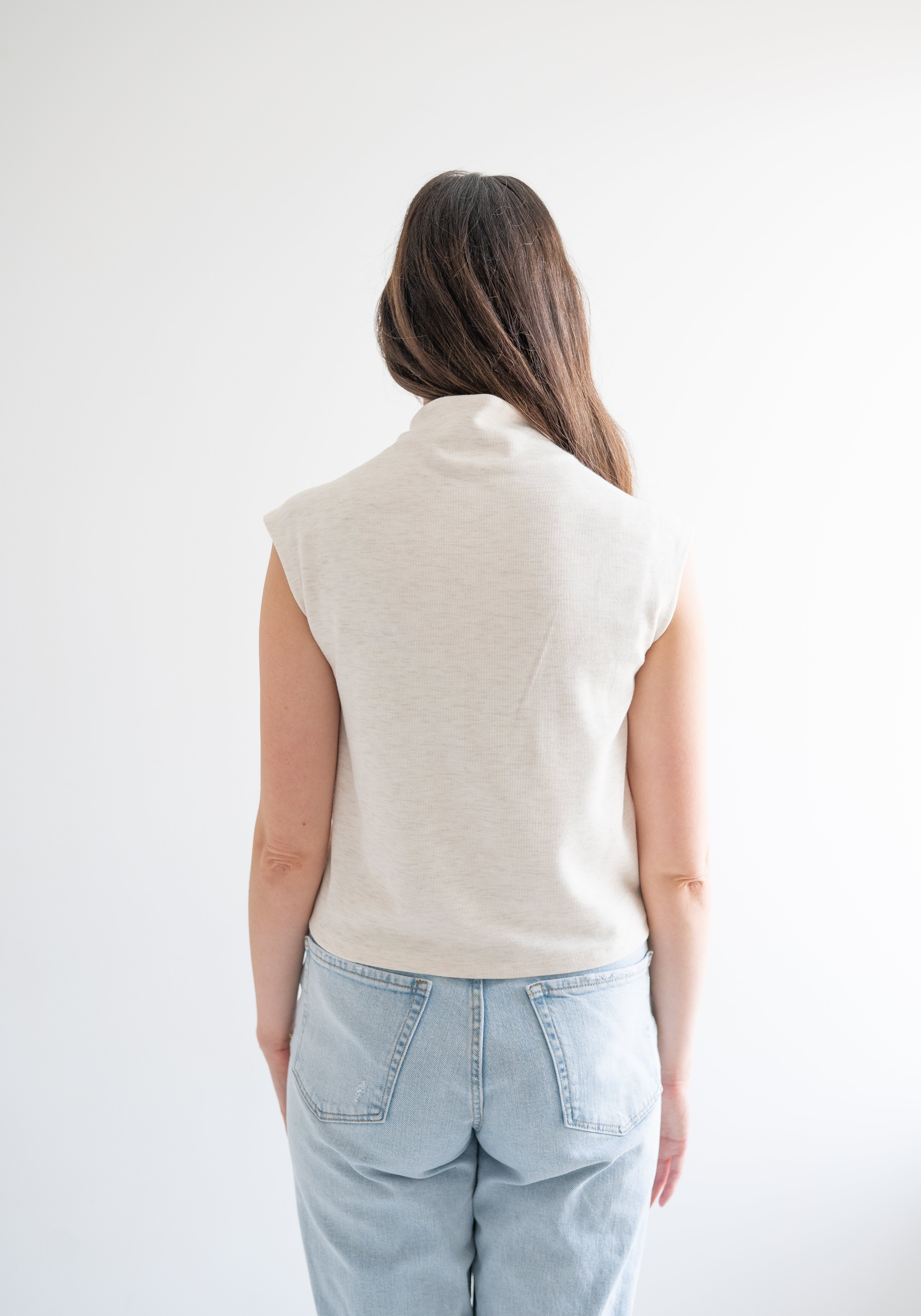 back view of woman wearing cream sleeveless mockneck sweater