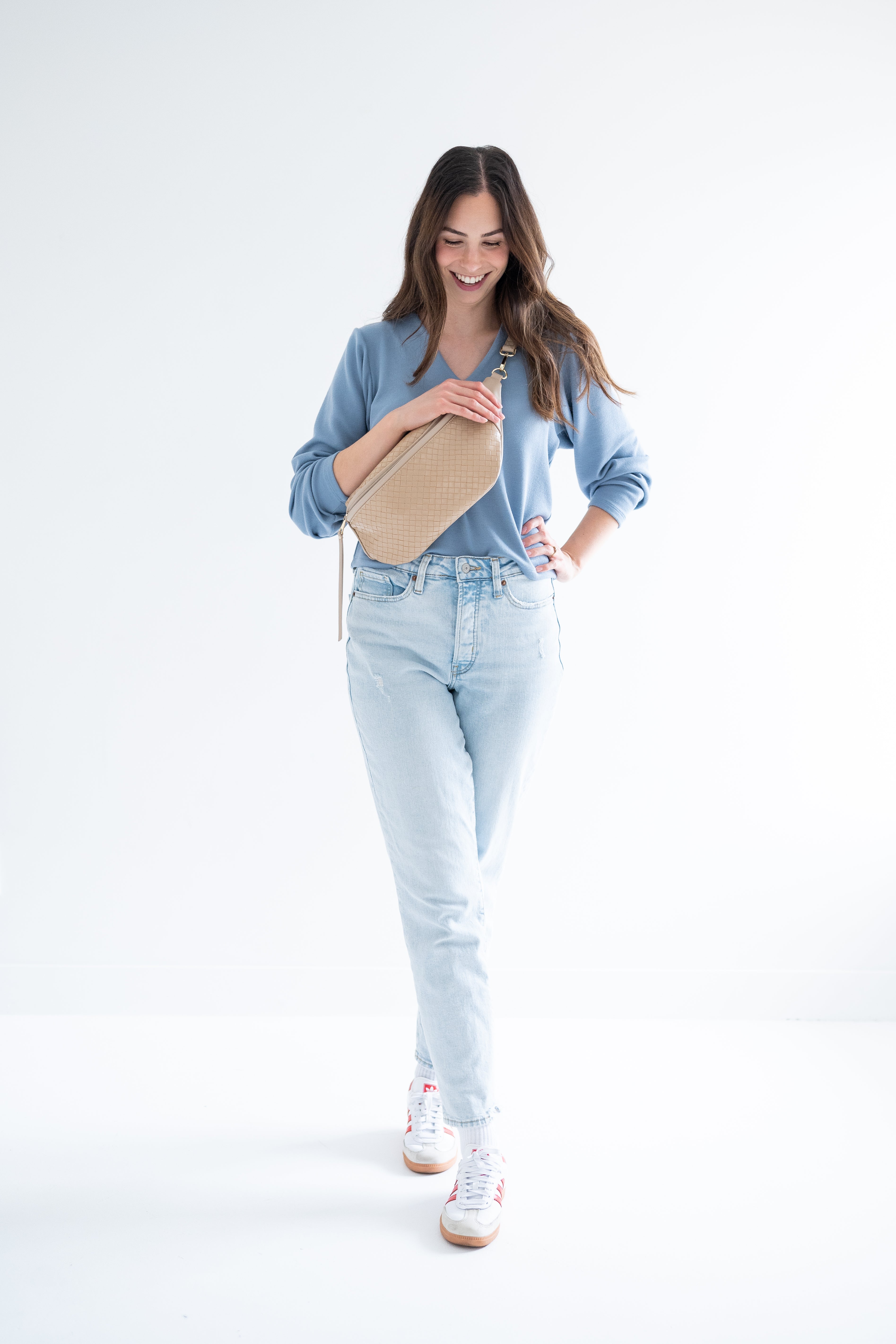 woman wearing blue v-neck sweater, fanny pack and light wash denim and sneakers