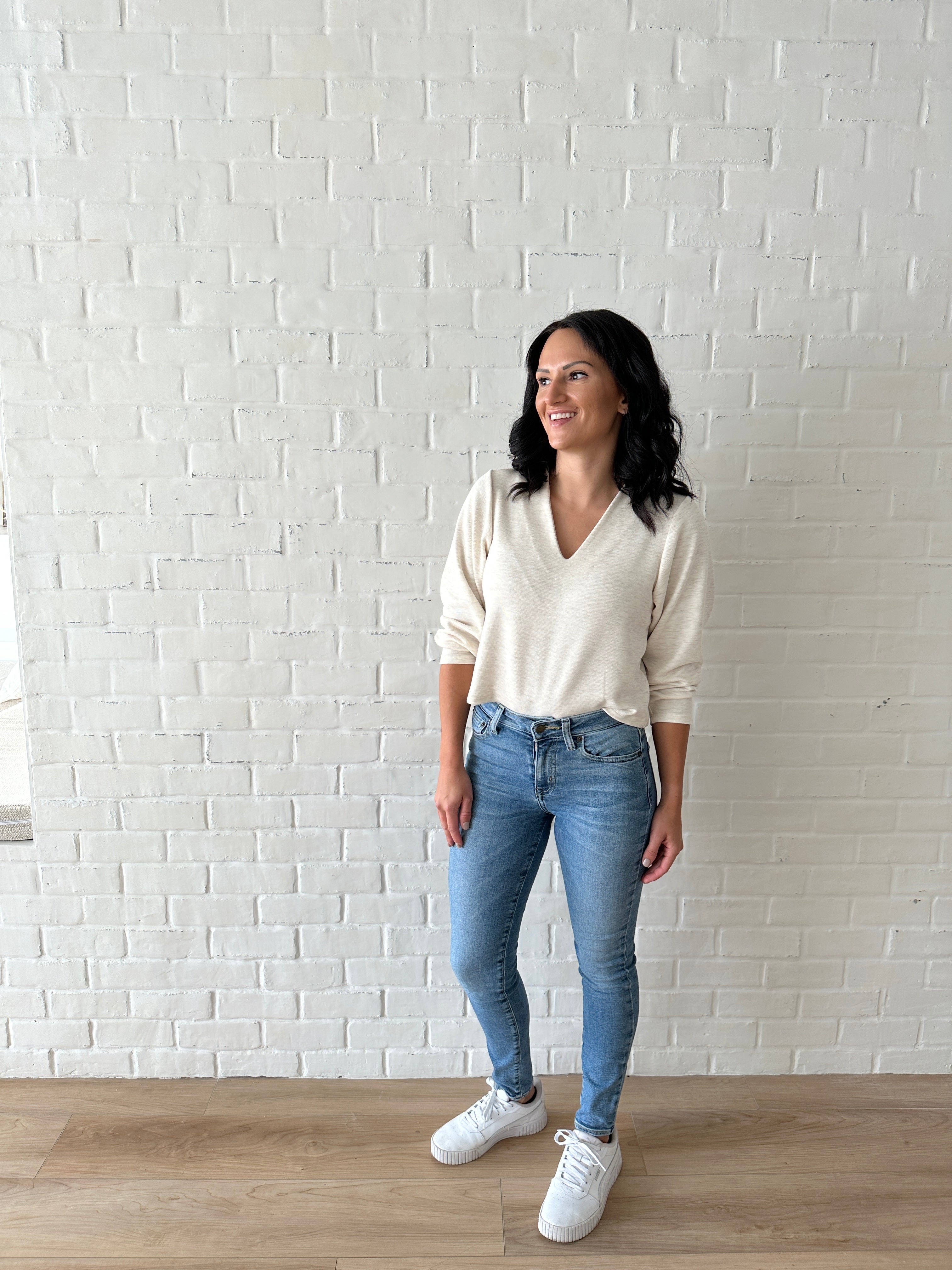 woman wearing cream v-neck sweater and jeans with sneakers